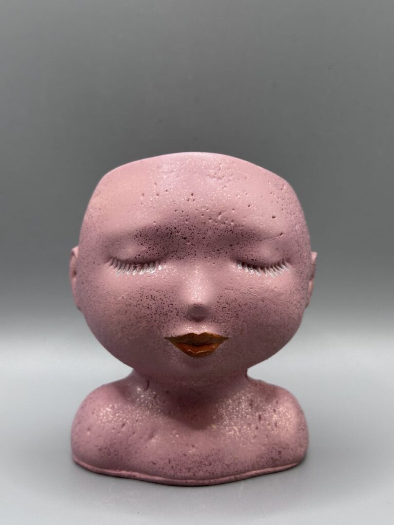 A detailed profile of a feminine face planter with refined features, hand-finished in a metallic rose quartz pink shimmer against a clean grey background.