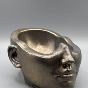 A detailed profile of a feminine face planter with refined features, hand-finished in a weathered bronze metallic texture against a clean grey background.