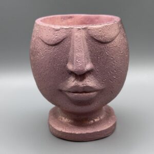 A whimsical feminine face planter with a golden flower in her hair, featuring a peach-toned top and an intricate purple geometric patterned base against a neutral background.