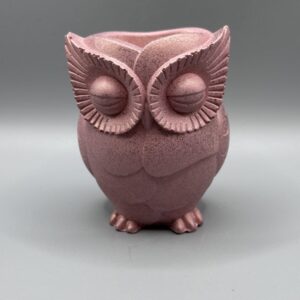A hand-finished owl planter with closed eyes and detailed feathers, rendered in a metallic rose quartz pink shimmer against a neutral grey background.