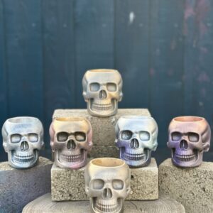 A collection of skull-shaped planters in various iridescent, gold, and silver finishes arranged on stone blocks.