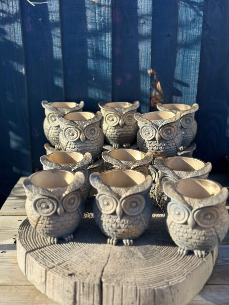 A highly detailed owl-shaped planter in an ancient gilded slate finish with metallic gold feather highlights, sitting on a natural wood stump