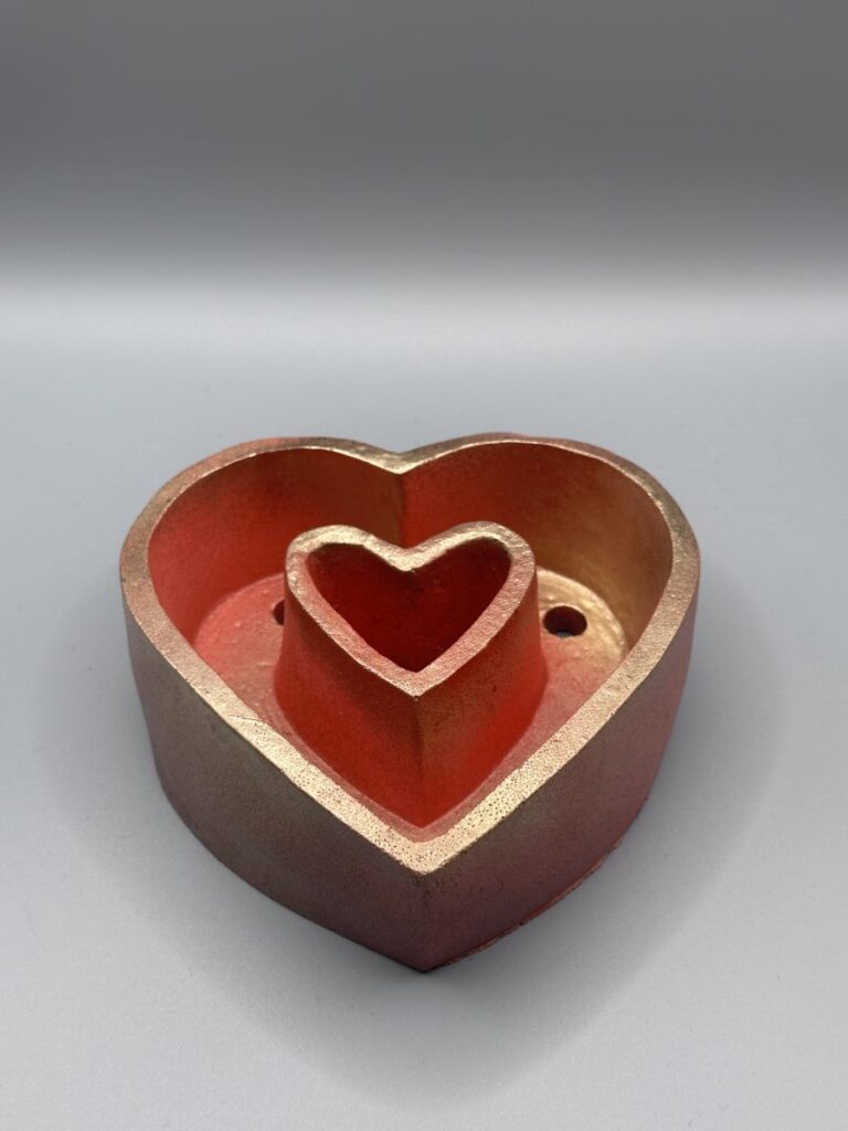 A unique dual-chambered nested heart planter featuring a crimson red exterior and a metallic gilded gold interior with two drainage holes, shown against a neutral background.