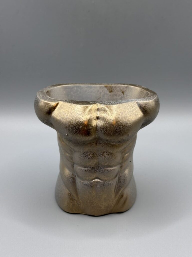 A sculptural male torso planter with a muscular physique, hand-finished in a Gilded Bronze Patina metallic texture against a clean grey background.