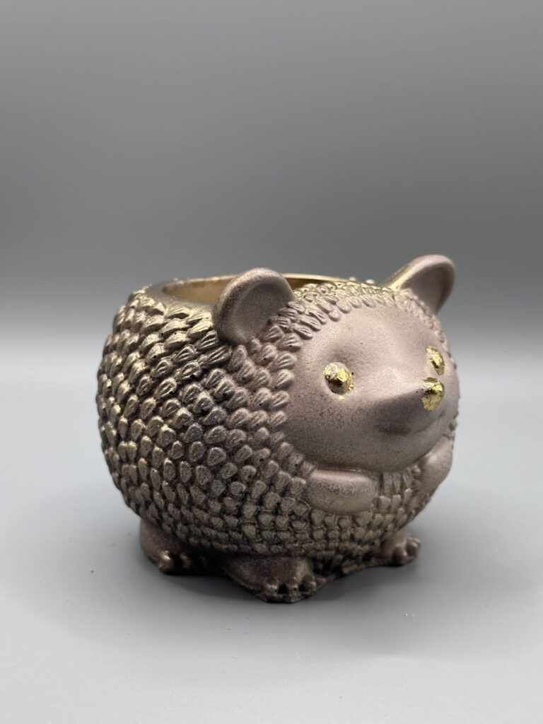 A small, round hedgehog planter with a warm metallic bronze-brown finish, detailed textured quills, and bright gold-leaf accents on the eyes and nose.