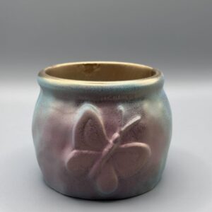 A small, rounded ceramic-style pot with an embossed butterfly on the side, featuring a pink and blue watercolor finish and a metallic gold rim.