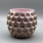 A round, dimpled plant pot with a metallic rose gold exterior and a soft pink interior, shown against a neutral grey background.