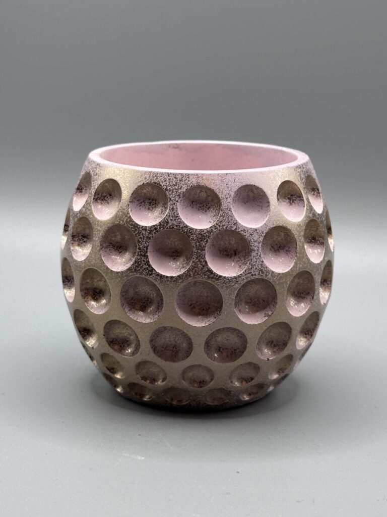 A round, dimpled plant pot with a metallic rose gold exterior and a soft pink interior, shown against a neutral grey background.