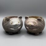 Two small, round hedgehog planters side-by-side; one is a metallic silver and the other is a metallic rose-bronze, both featuring textured quills and gold-leaf eyes and noses.