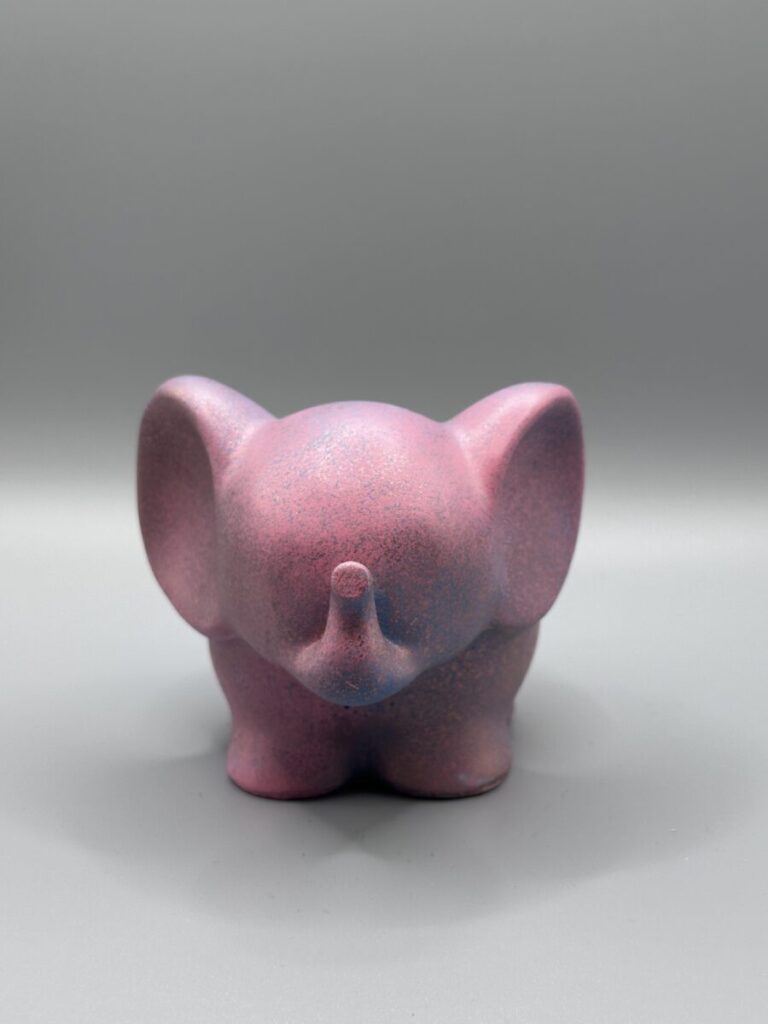 A side view of a small, matte mauve elephant planter with blue and copper speckles, standing against a clean grey background.