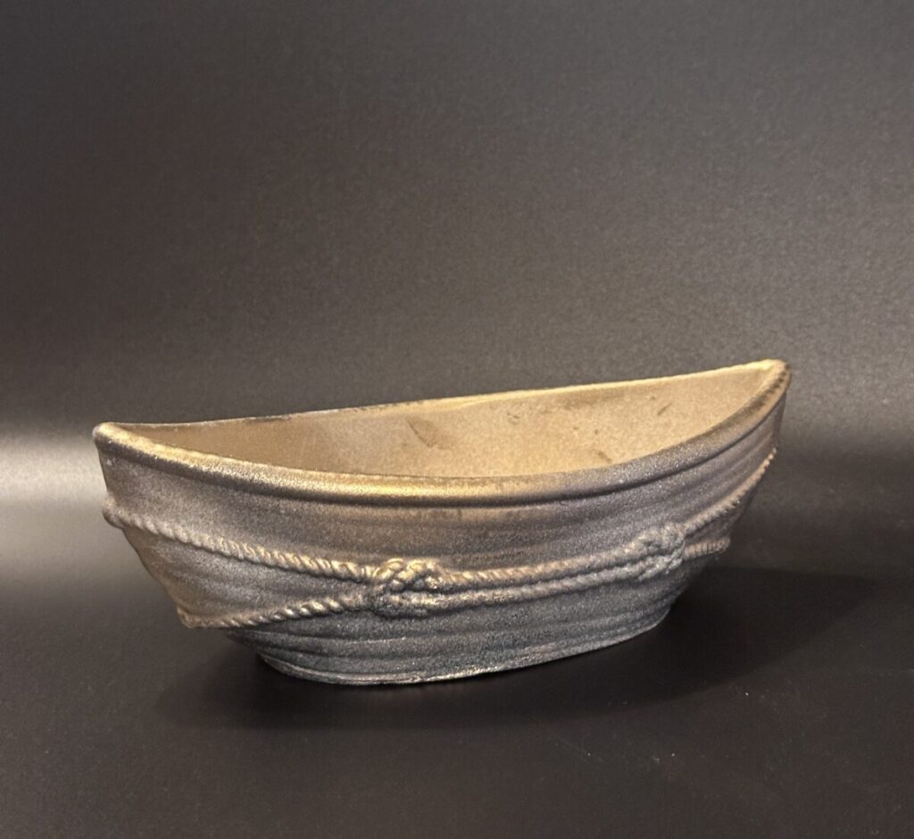 A boat-shaped ceramic vessel with a metallic golden-bronze glaze and raised rope textures, shown in two different lighting setups to highlight the shimmering finish.