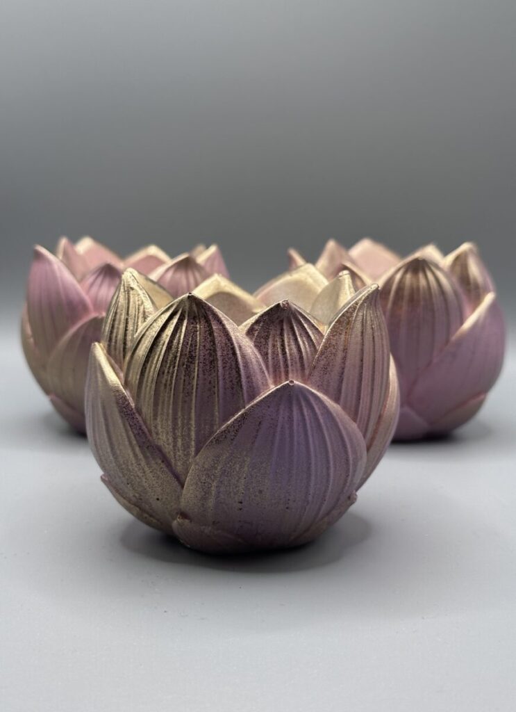 Three lotus-shaped planters in a gradient of dusty pink and metallic gold, arranged on a neutral grey background.