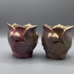 Two small, ornate planters shaped like lotus flowers with a textured rose and gold metallic gradient finish, displayed on a grey surface.