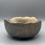 A dark gunmetal gray hand-cast planter bowl with a metallic sheen and an irregular, wavy top edge, centered against a neutral gray background.