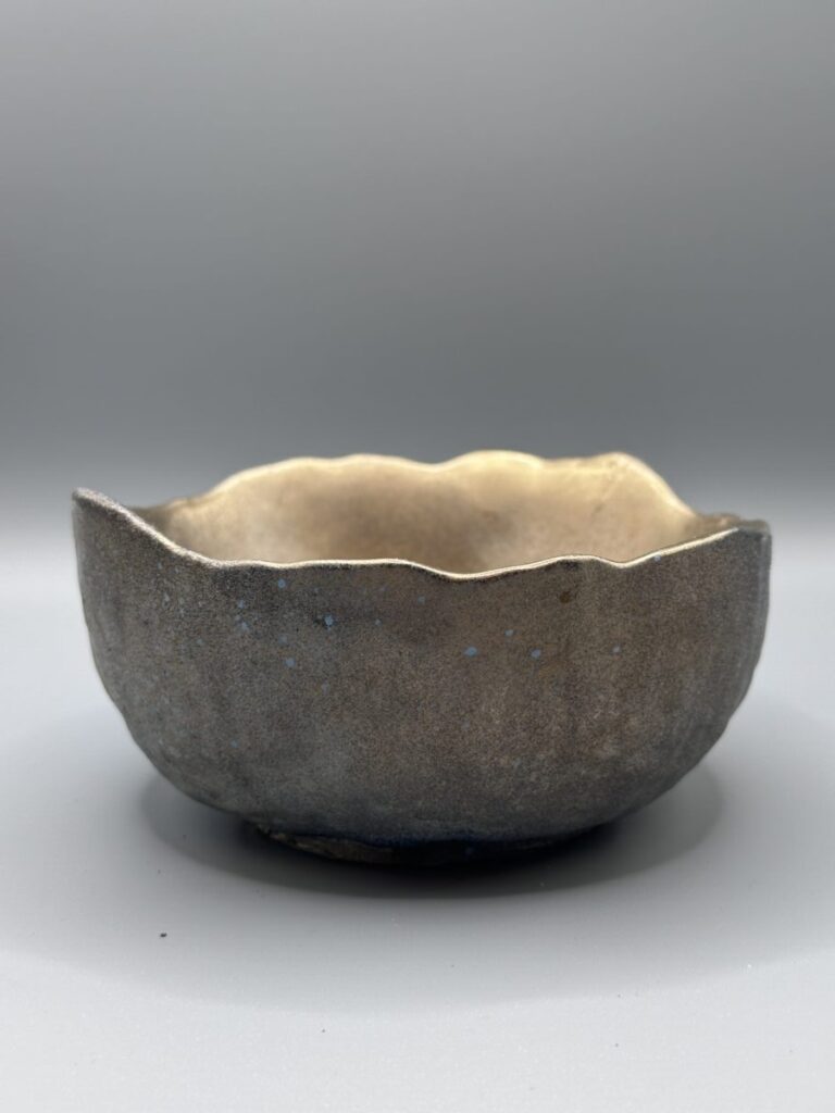 A dark gunmetal gray hand-cast planter bowl with a metallic sheen and an irregular, wavy top edge, centered against a neutral gray background.