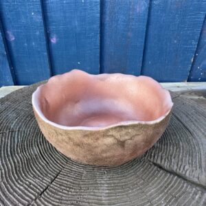 A wide, shallow hand-cast planter bowl with a rustic terracotta color and an irregular, wavy rim, displayed on a textured dark wood surface against a blue wooden backdrop.