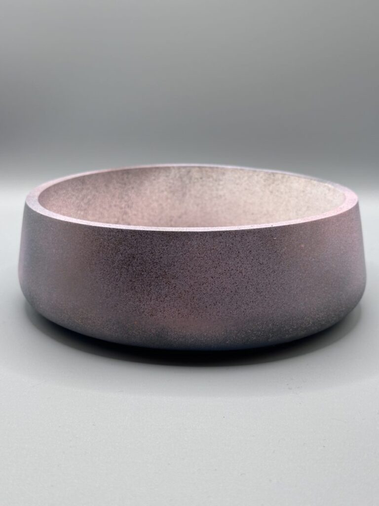 A wide, shallow round planter with a dark, speckled texture transitioning from a charcoal base to a deep purple iridescent rim.