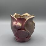 Two small, ornate planters shaped like lotus flowers with a textured rose and gold metallic gradient finish, displayed on a grey surface.