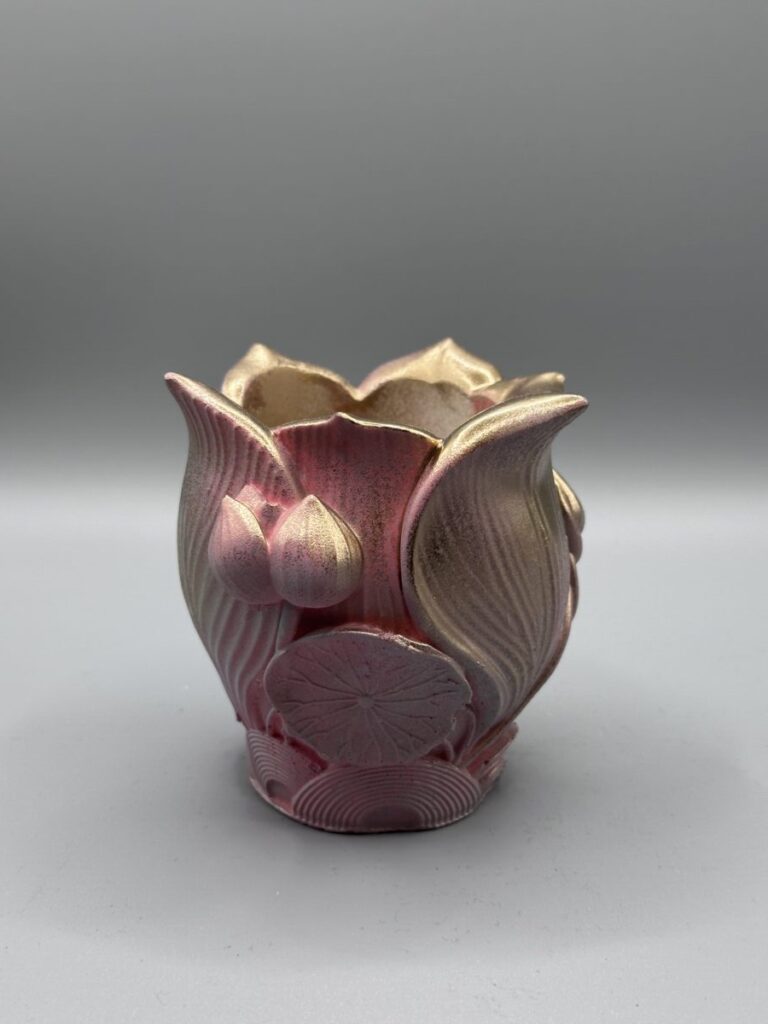 Two small, ornate planters shaped like lotus flowers with a textured rose and gold metallic gradient finish, displayed on a grey surface.