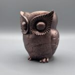 A front-facing view of a handcrafted owl planter with a deep metallic bronze finish, featuring detailed fanned patterns around the eyes and a textured surface.
