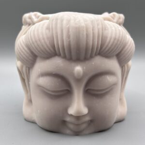 A close-up of a sculptural plant pot shaped like a serene face with closed eyes and detailed swept-back hair, featuring a smooth matte off-white finish against a grey background.