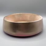 A low-profile round planter with a color gradient shifting from a matte pink base to a metallic gold top, centered on a grey background.