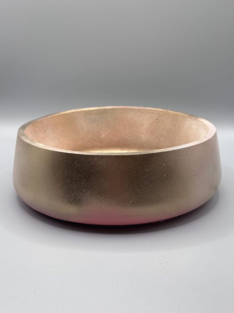 A low-profile round planter with a color gradient shifting from a matte pink base to a metallic gold top, centered on a grey background.