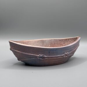 A boat-shaped ceramic vessel with a metallic copper and blue glaze, featuring raised rope textures around the exterior, set against a neutral grey background.