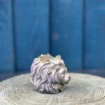 Close-up of a stone lion head planter with an iridescent green and purple shimmer, sitting on a wooden tree stump background.