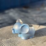 A small, light blue elephant-shaped planter with a shimmering, glittery gold and blue texture sitting on a rustic wooden tree stump.