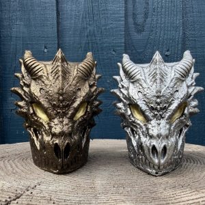 Hand-cast dragon skull planter in antique silver with amber eyes and curled horns, on a wooden log