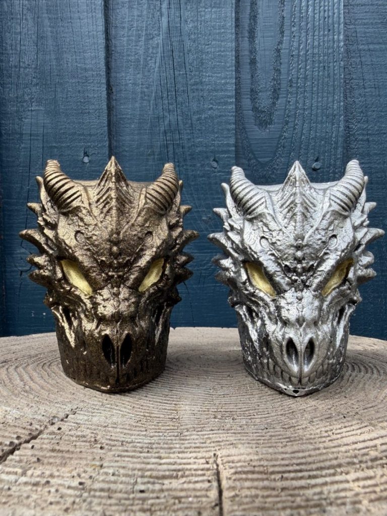 Hand-cast dragon skull planter in antique silver with amber eyes and curled horns, on a wooden log