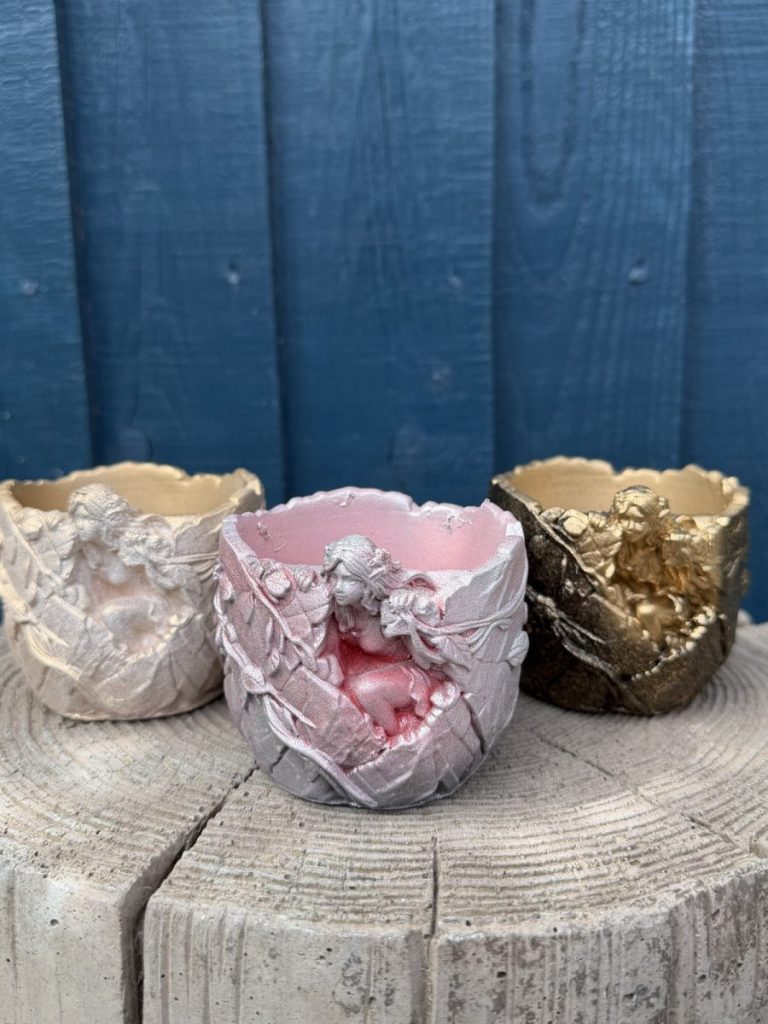 Hand-cast fairy planter in blush pink, a sleeping fairy wrapped in cast leaves, on a wooden log