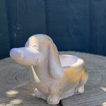 Hand-cast long-eared puppy planter in pearl white, head raised with ears hanging down, on a wooden log
