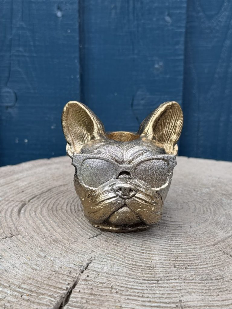 Hand-cast French bulldog planter in antique gold with a silver face, wearing sunglasses, on a wooden log