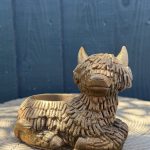 Hand-cast Highland cow planter in antique gold, shaggy coated and lying down with a planting well in its back, on a wooden log