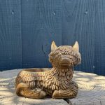 Hand-cast Highland cow planter in antique gold, shaggy coated and lying down with a planting well in its back, on a wooden log