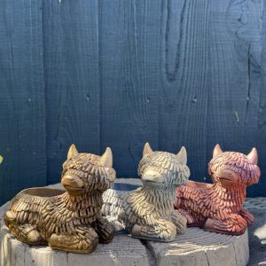 Hand-cast Highland cow planter in antique gold, shaggy coated and lying down with a planting well in its back, on a wooden log
