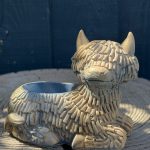 Hand-cast Highland cow planter in antique silver, shaggy coated and lying down with a planting well in its back, on a wooden log