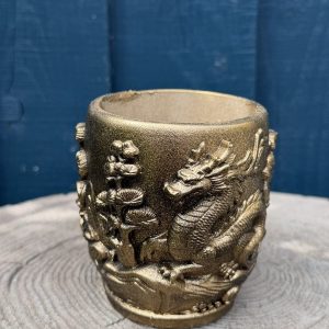 Hand-cast barrel planter in burnished antique gold with a raised oriental dragon and blossom relief, on a wooden log