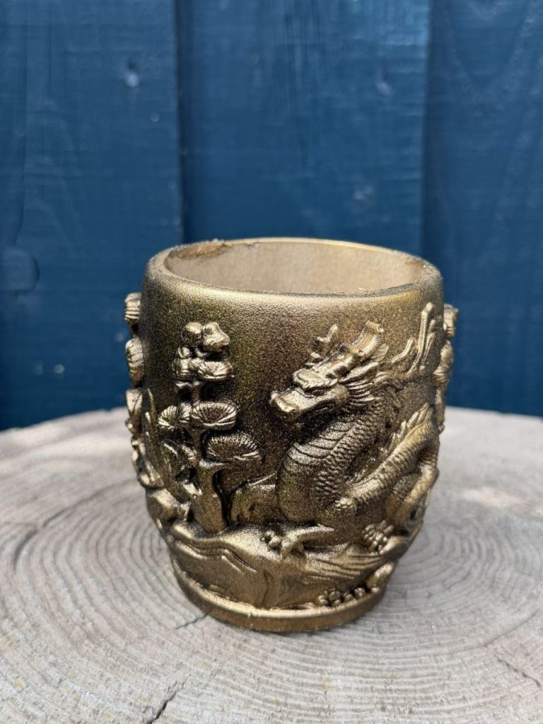 Hand-cast barrel planter in burnished antique gold with a raised oriental dragon and blossom relief, on a wooden log
