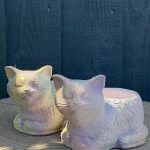 Hand-cast sleeping cat planter with an iridescent opal pearl finish, curled up with eyes closed, on a wooden log