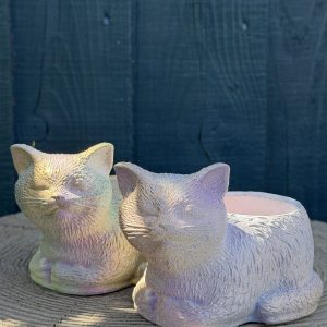 Hand-cast sleeping cat planter with an iridescent opal pearl finish, curled up with eyes closed, on a wooden log