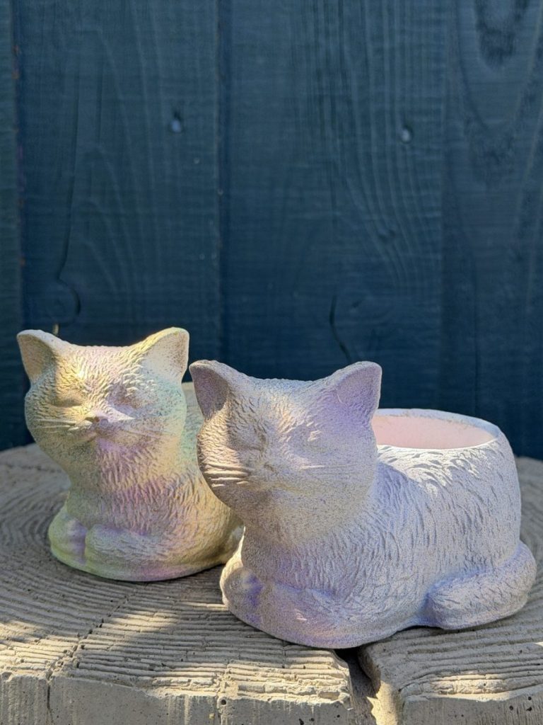 Hand-cast sleeping cat planter with an iridescent opal pearl finish, curled up with eyes closed, on a wooden log