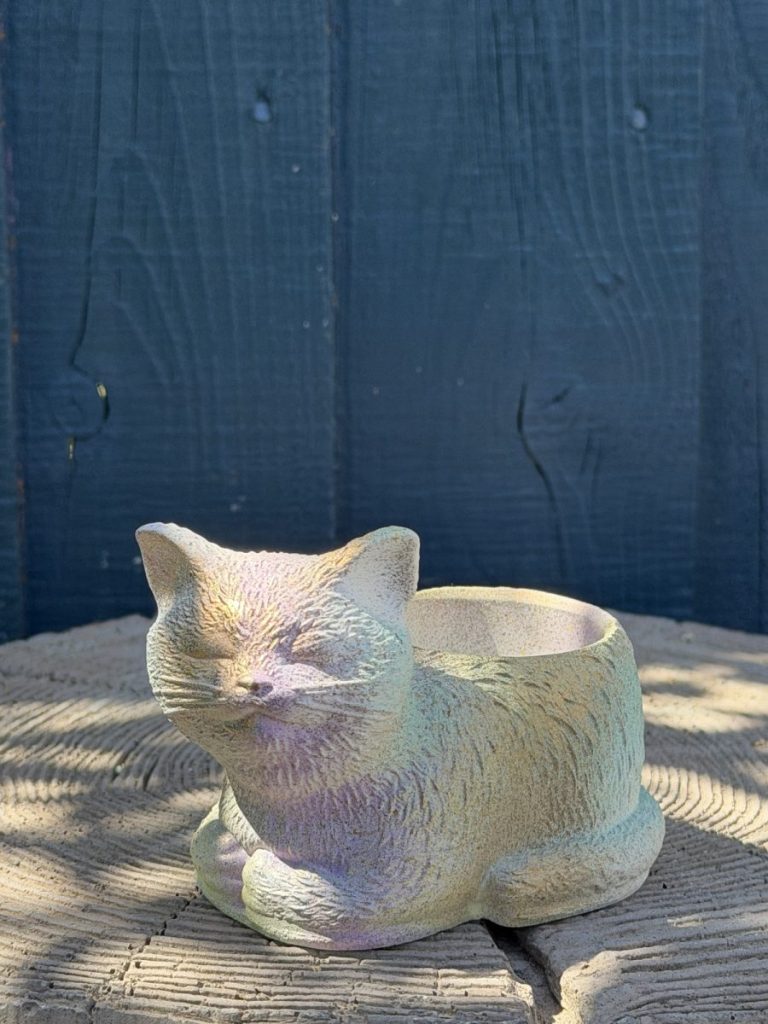 Hand-cast sleeping cat planter with a green-tinted iridescent finish, curled up with eyes closed, on a wooden log