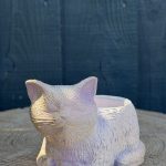 Hand-cast sleeping cat planter with an iridescent opal pearl finish, curled up with eyes closed, on a wooden log